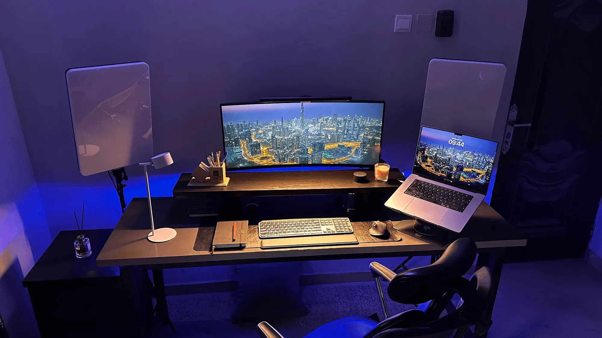 A desk setup in blue light: an ultrawide monitor and a laptop on a stand